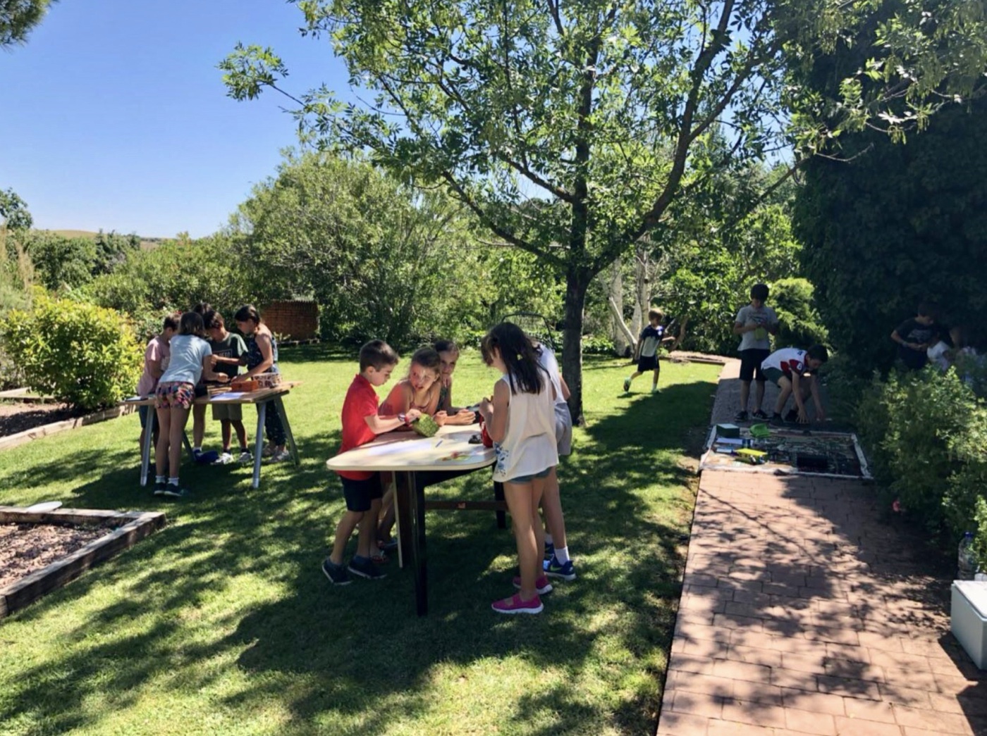 Escape room a domicilio Picapista al aire libre en jardín privado en Madrid: equipos de niños jugando en mesas exteriores rodeados de naturaleza